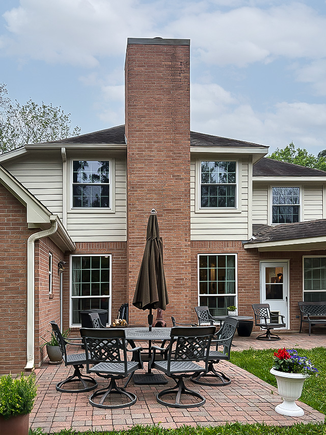 Houston Woodland Home with brick chimney and patio furniture set on a paved area.