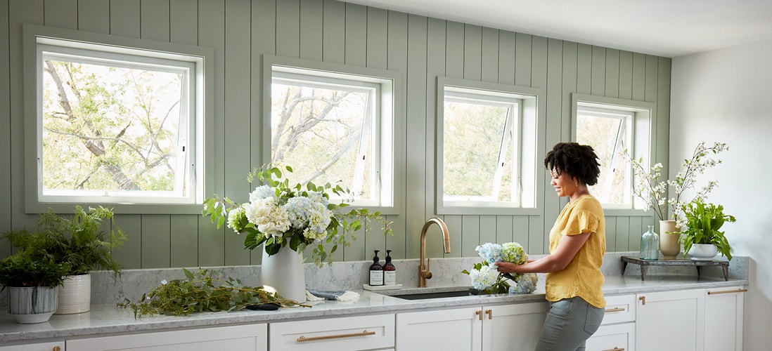 woman in a yellow shirt standing in kitchen by four awning windows