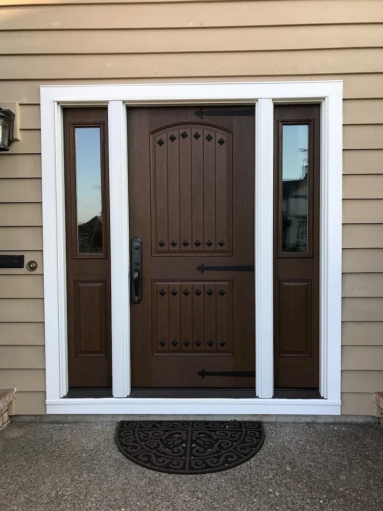A brown front door has decorative clavos and hinge straps, with a half light sidelight on each side.