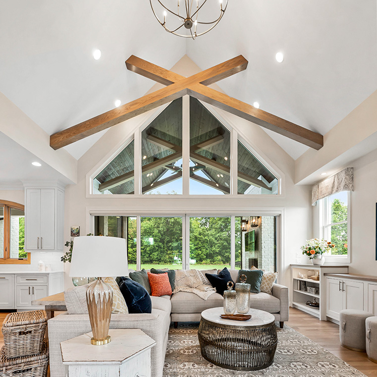 Open-concept living room with wood floors, vaulted ceiling, large windows, and stylish decor