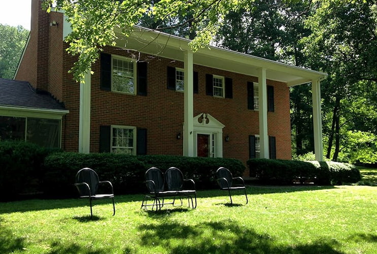 Victorian brick home with four pillars, white windows and black shutters