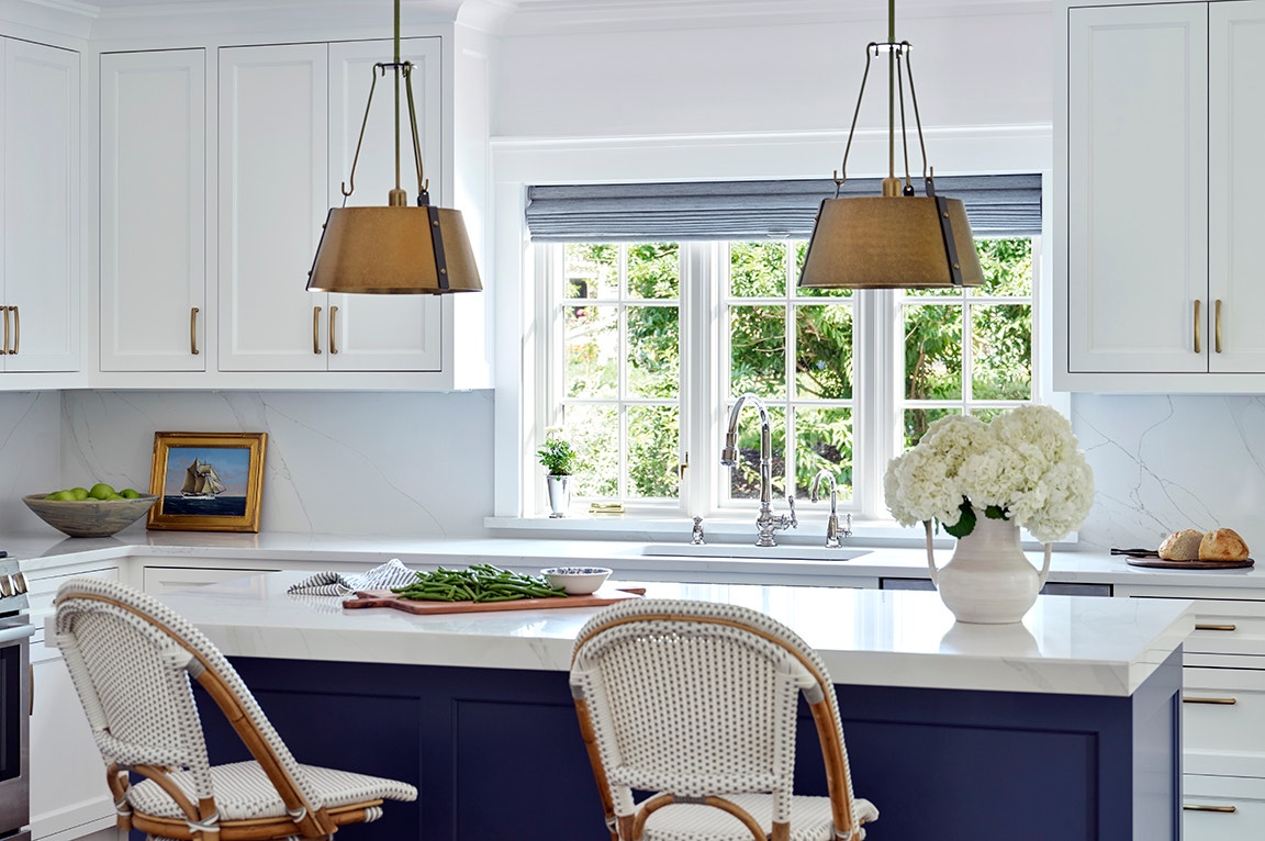 Large over-the sink windows complement a modern kitchen with white cabinets and a central island.
