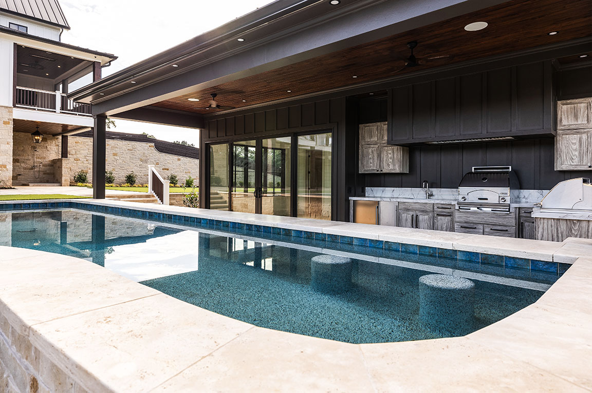Modern pool house with outdoor kitchen and sliding glass doors.
