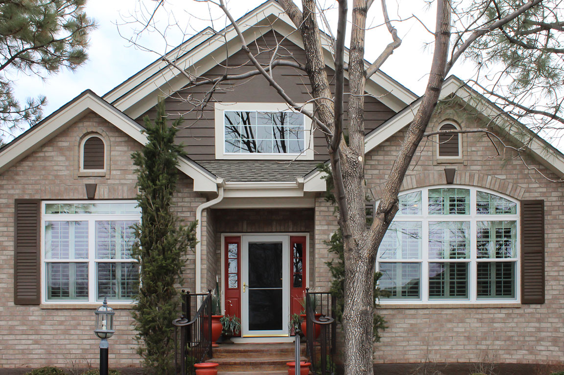A modern home exterior featuring large vinyl windows, brick facade, and landscaped entrance.