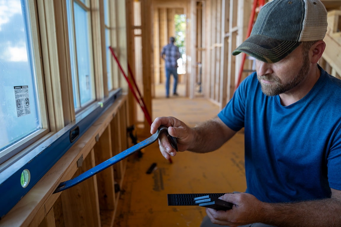 A contractor is setting shims underneath a newly installed window onto a wall.