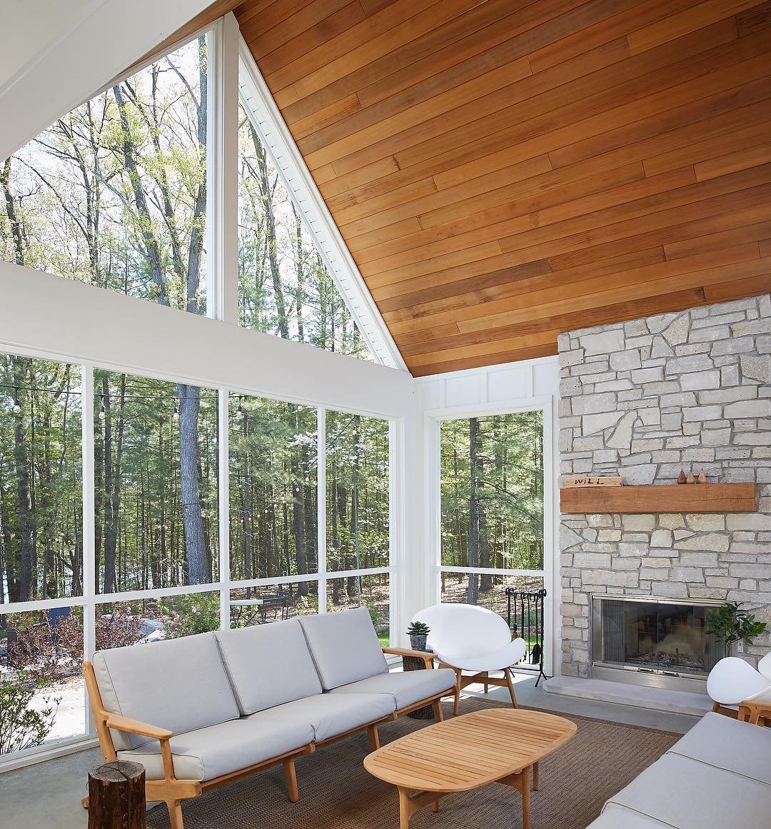 mid-century living room looks out to wooded backyard through wall of windows with triangle windows near ceiling