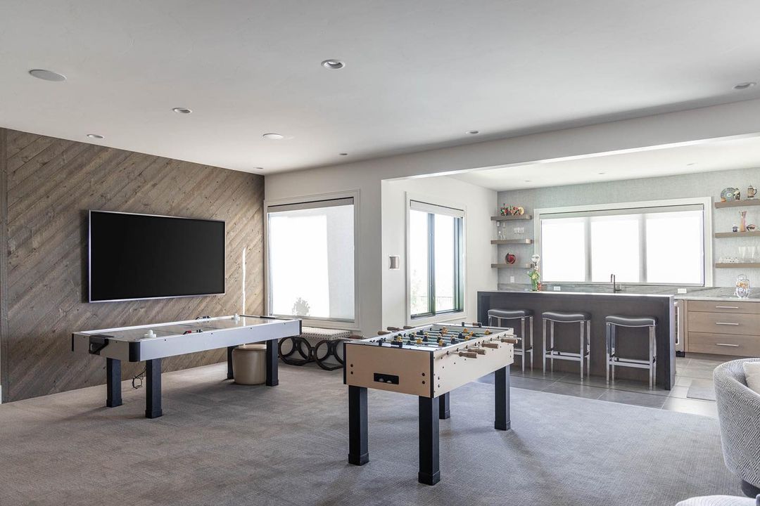 A lower-level game room features an air hockey and foosball table with walkout basement windows as the backdrop.