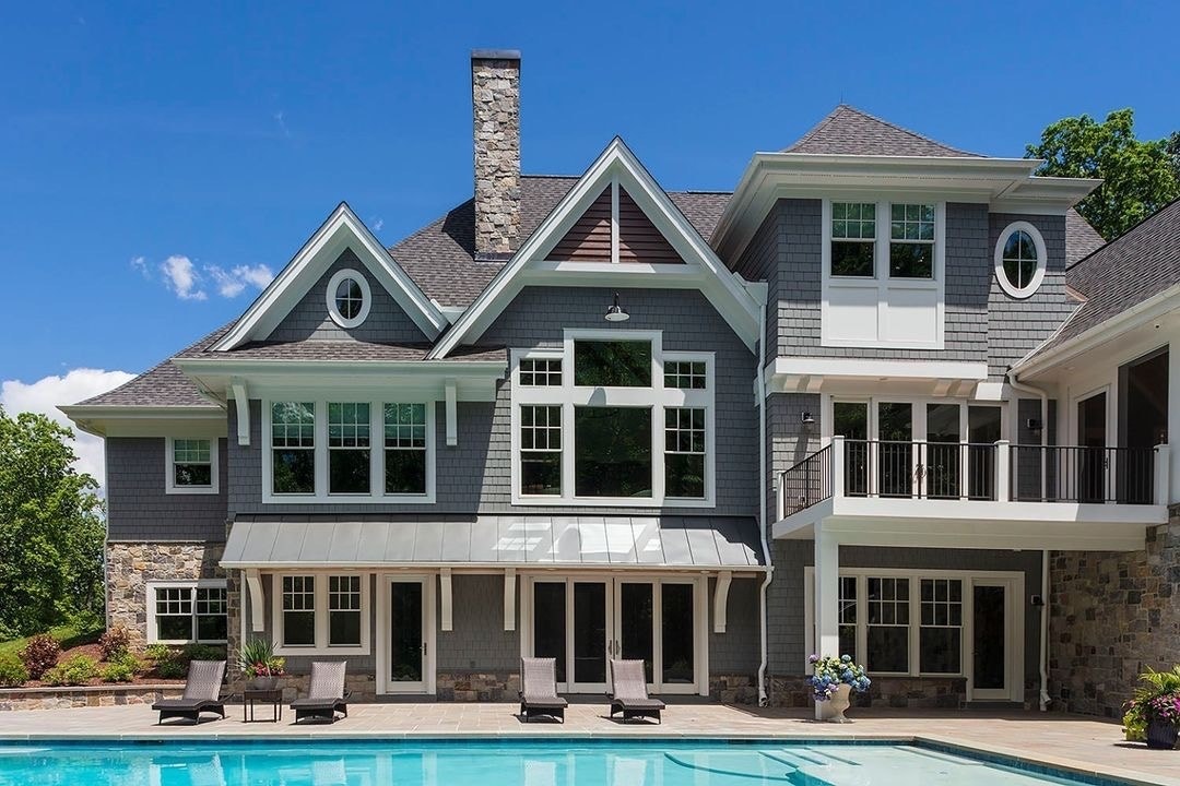 The back of a gray house with white windows and doors overlooks a backyard pool.