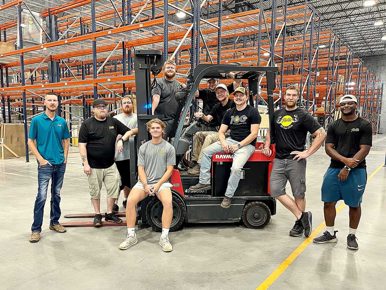 Kansas Pella Careers team posing with a forklift in a large warehouse.