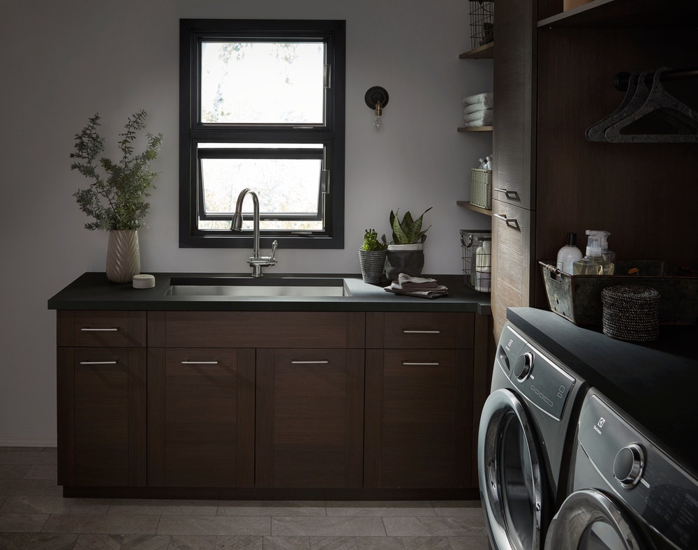 Laundry room with dark wood cabinets, black stacked awning windows, and gray washer and dryer