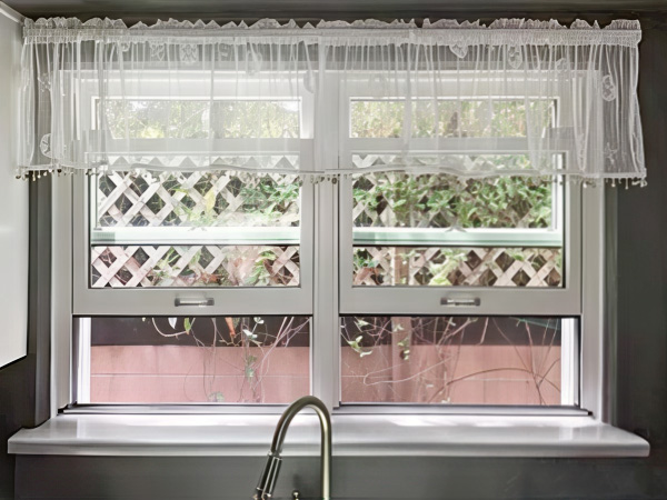 Two windows with a sheer valance over a kitchen sink with retractable screens.