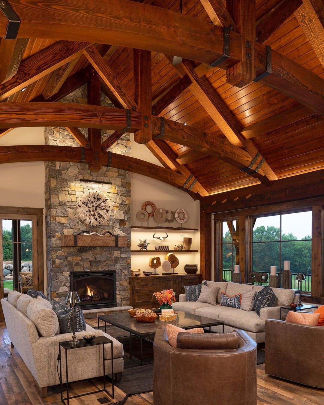 Wood windows and a patio door surround a cozy living room with wood beams and a stone fireplace.
