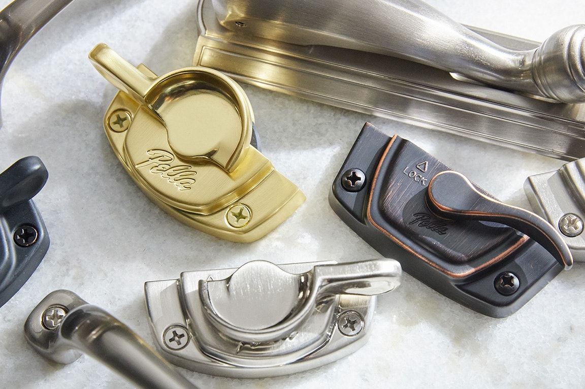 A collection of various window hardware pieces in brass, nickel, and black finishes, showcasing intricate designs.