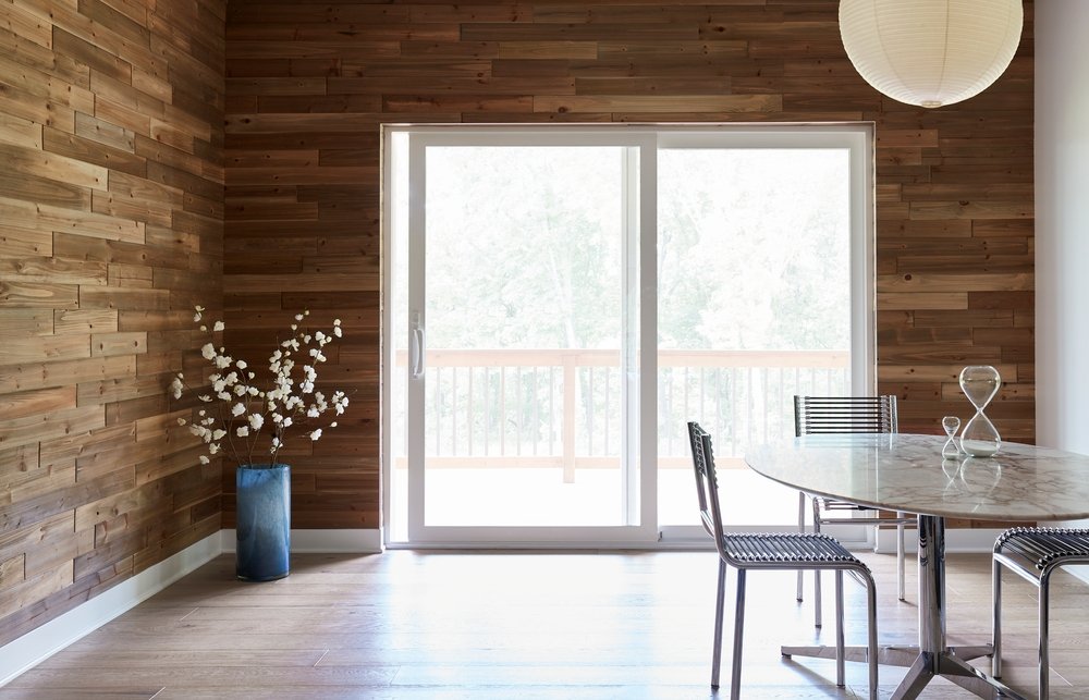 Dining room with wood plank walls, table and chairs, and white vinyl sliding patio door