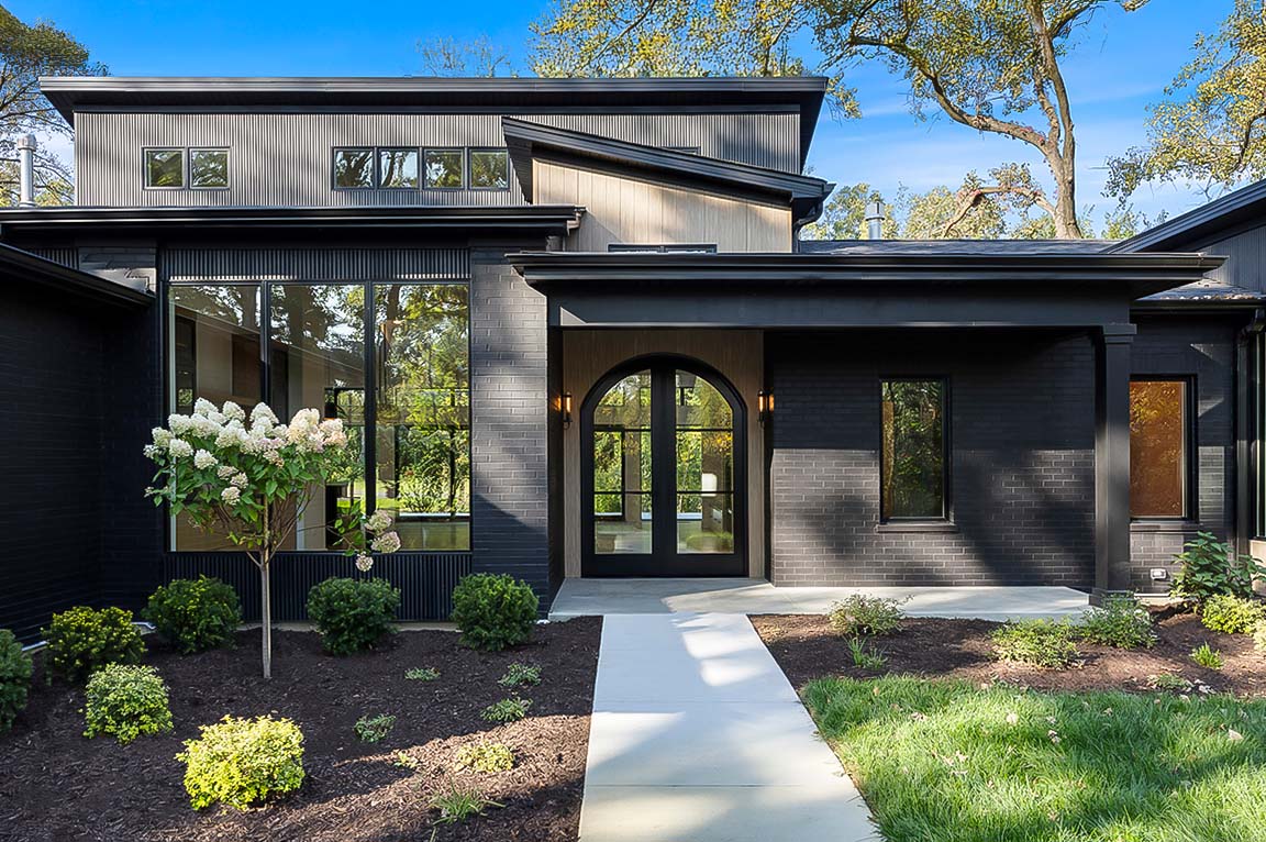 Modern black home exterior with arched front entry, large windows, and landscaped walkway.