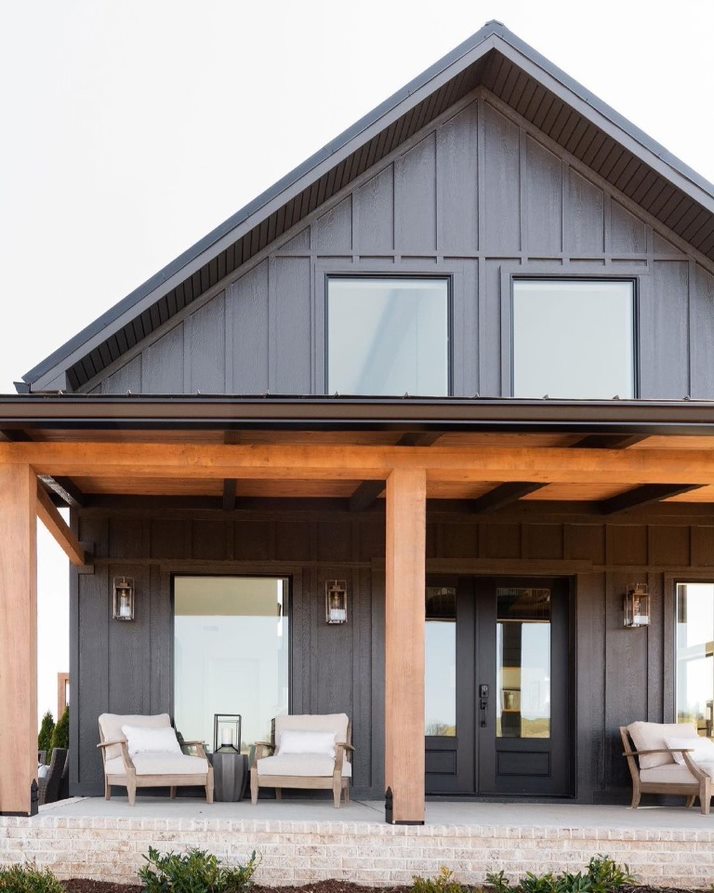 A modern farmhouse with black siding and black picture windows has a cozy porch out front.