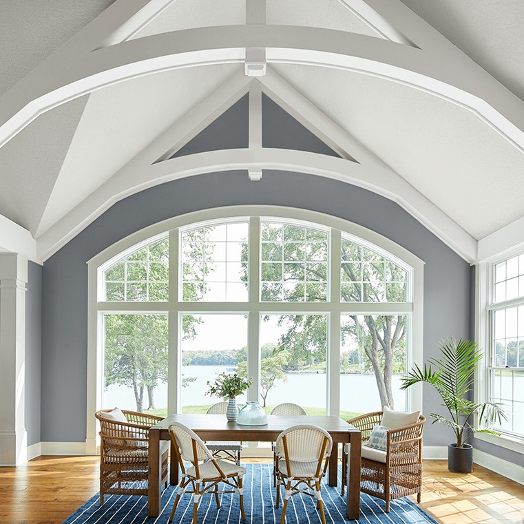 A modern living room with a white traditional window, featuring a wooden table and wicker chairs, overlooking a scenic view.