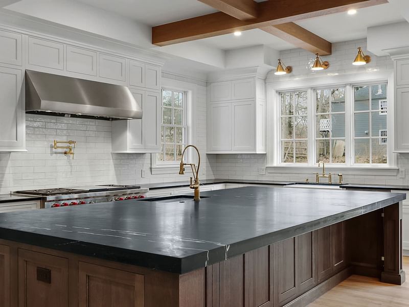 A large kitchen with white windows and a large black countertop.