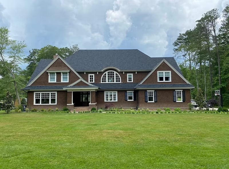 The exterior of a brown craftsman house has white windows, including an arch window in the center.