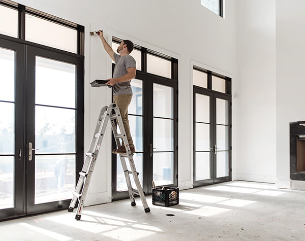 a contractor is putting the finishing touches of paint on a newly-installed set of french doors.