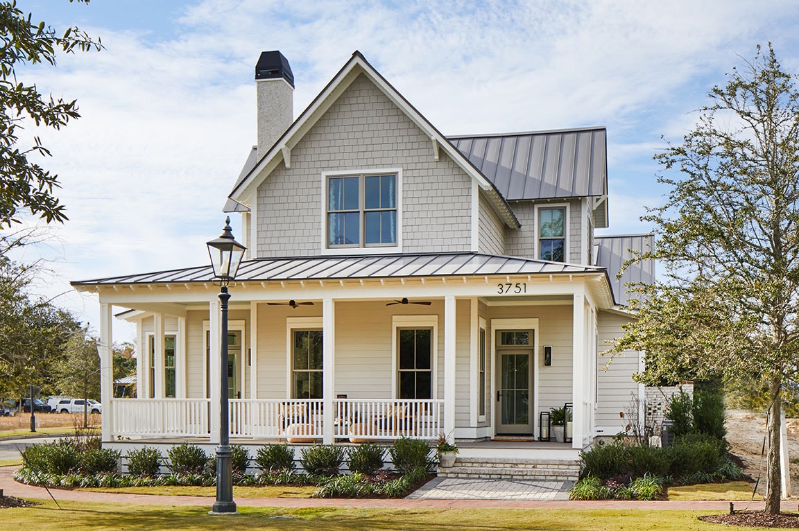 Modern farmhouse home exterior with white siding, wraparound porch, black metal roof, and large energy‑efficient windows.
