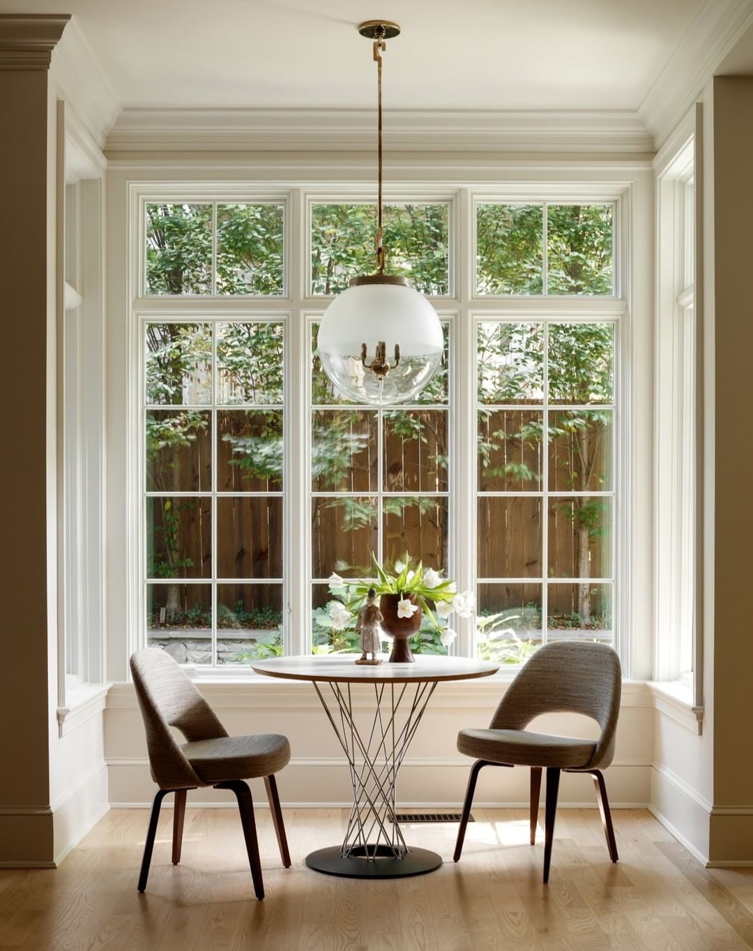 A breakfast nook features a small table with two chairs and white windows with grilles as the backdrop.