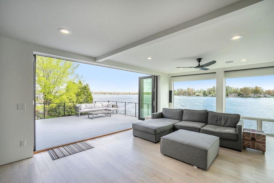 A lakefront room with a couch features an accordion patio door that opens to the deck.