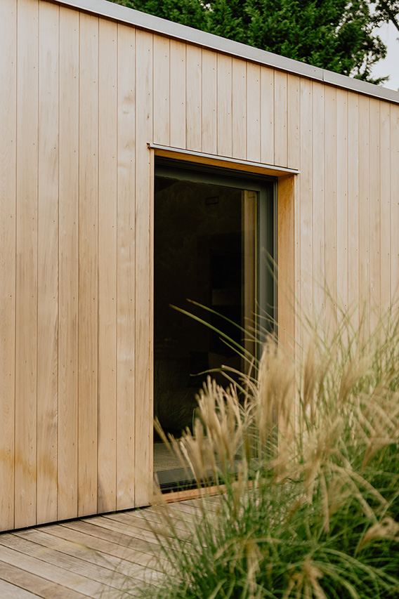 A large energy efficient window set in a modern light wood exterior with tall grass in the foreground.
