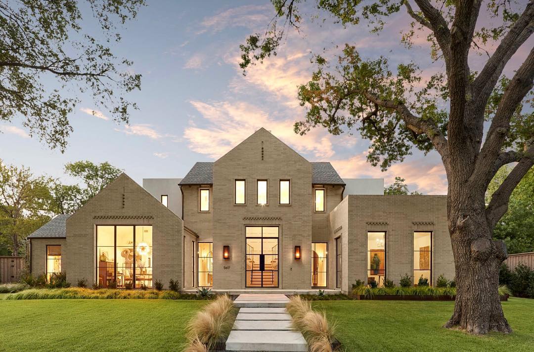 tan modern home at dusk with large windows and doors lit up