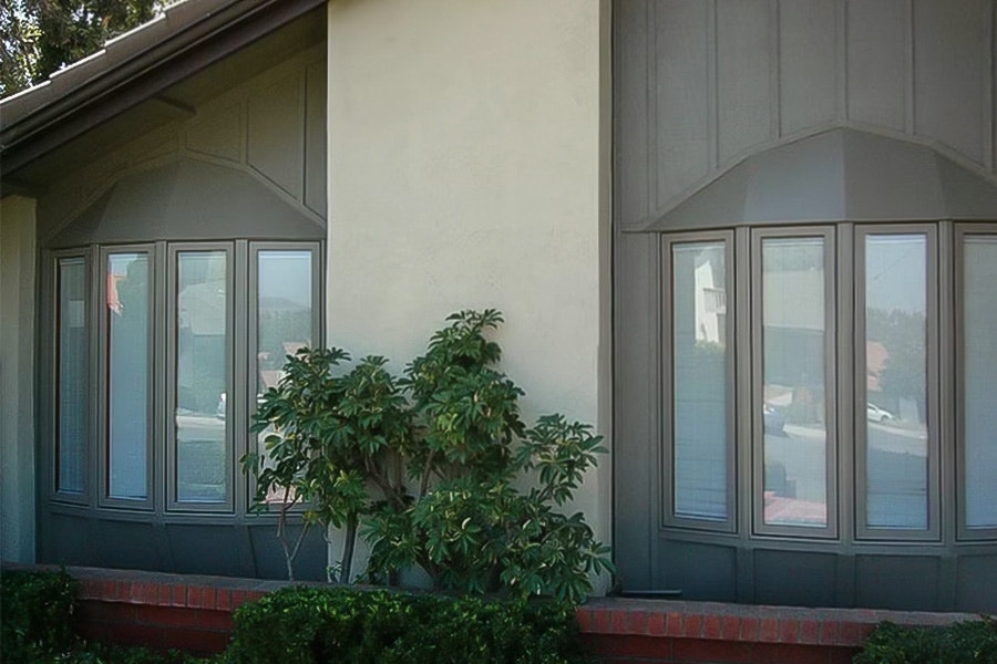 A modern home exterior featuring a bow window replacement with a lush green shrub in front.