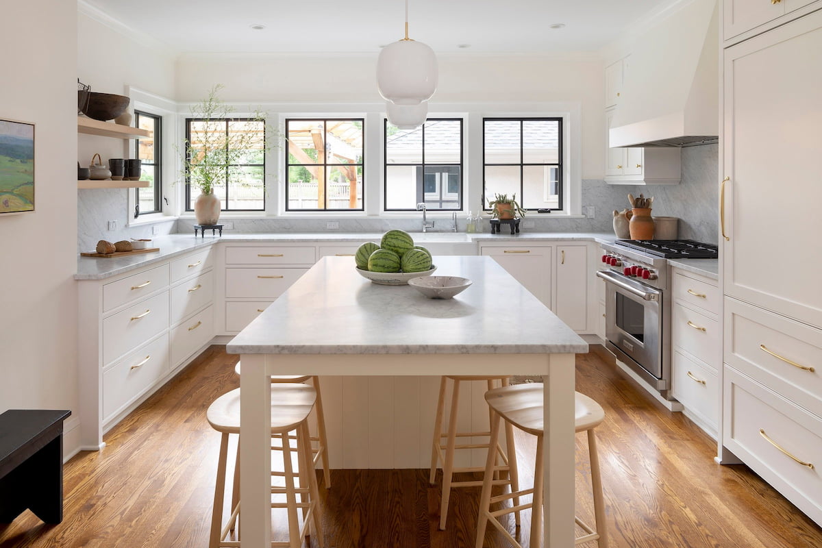 A kitchen with white cabinets has kitchen window backsplash on the far wall.