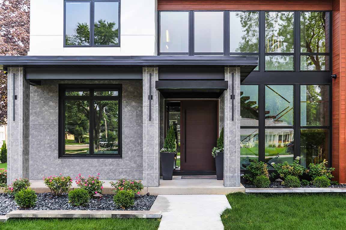 Modern home entry with black-framed windows, stone columns, and minimalist landscaping.