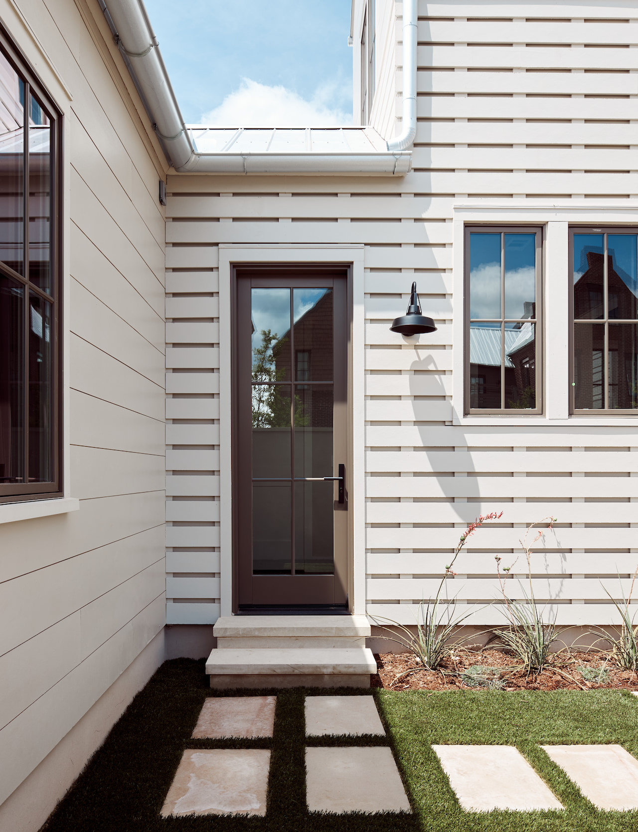 A brown hinged door on a white home leads to the backyard with stepping stones as the path.
