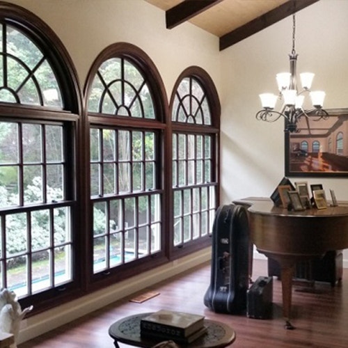 Wall of mahogany windows with half circle transoms above in piano room