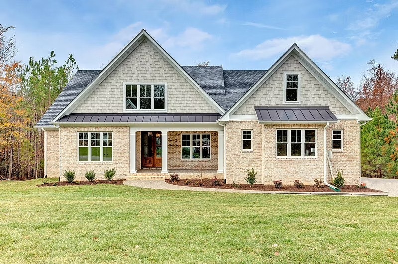 A farmhouse-style home has tan siding and stonework, and features white double-hung windows with grilles throughout.