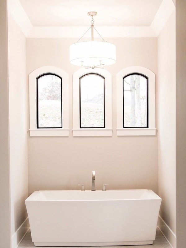 Three arched windows with black trim in a nook above a white bathtub