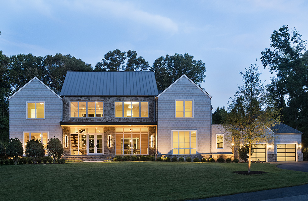 Modern farmhouse with large windows and gray siding at dusk