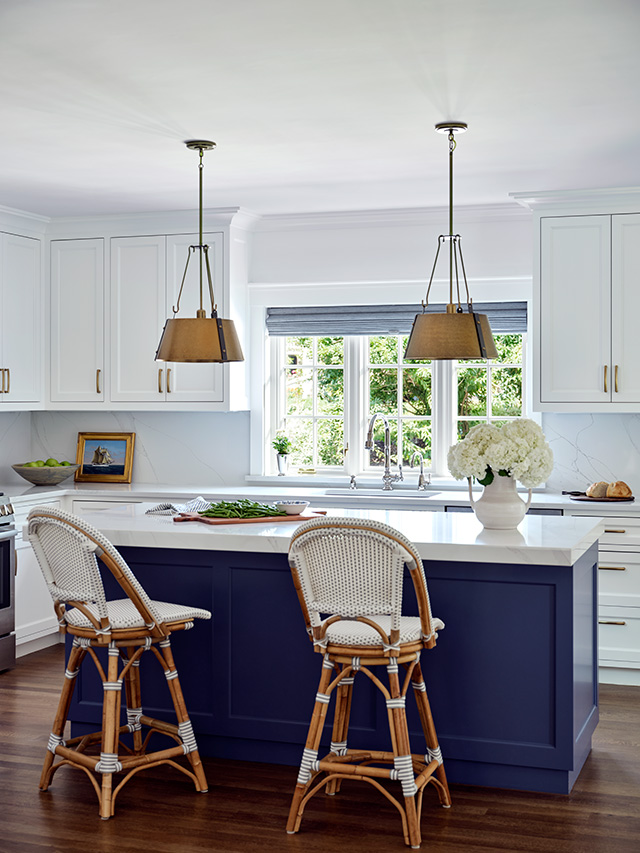 A modern kitchen with a colored island, white cabinets, and stylish kitchen windows, featuring two rattan bar stools. 