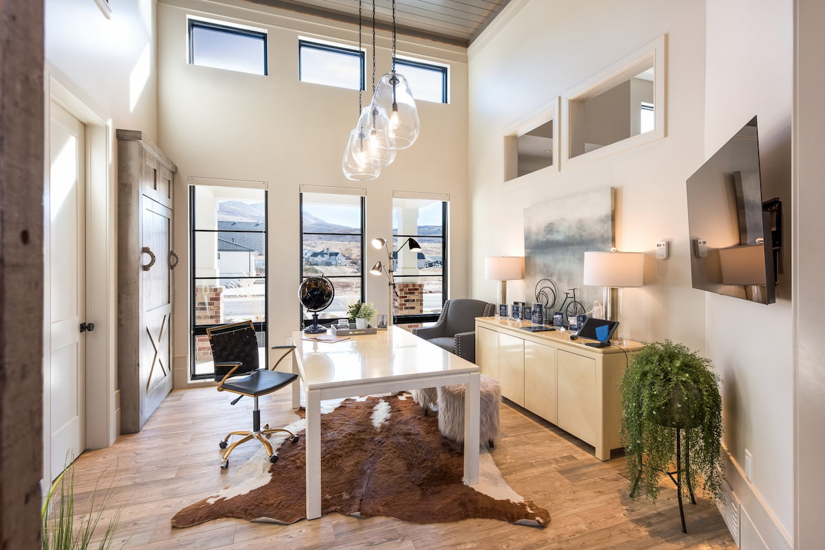 Home office windows on the back wall let natural light into this room with a desk, chair and hanging light fixtures.