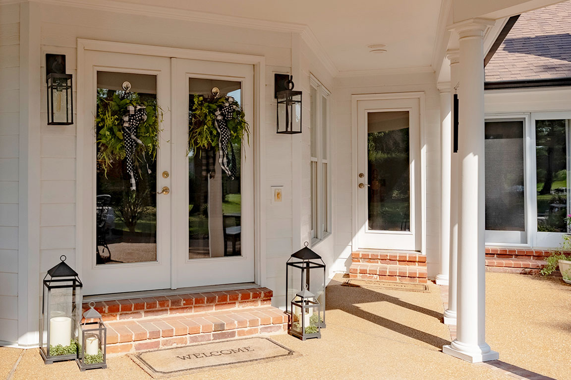White hinged doors with full glass panel and silver handle on white siding exterior.