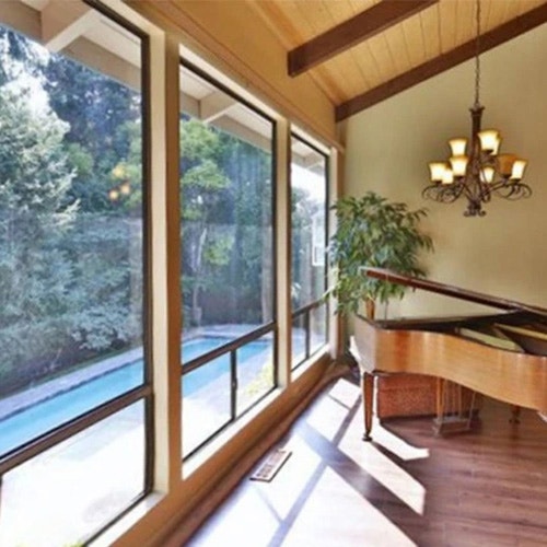 A spacious living room with large windows, a grand piano, and a view of greenery, showcasing before brown window.