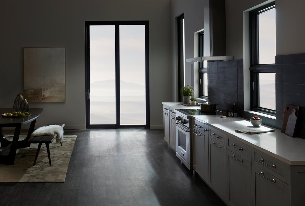 Dark and contemporary kitchen with black sliding patio door and a wall of cabinets with awning windows above