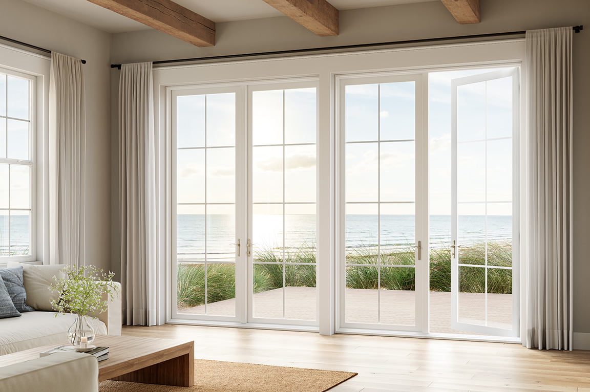 Bright living room featuring white French patio doors with grille patterns and a view of water and coastal landscaping.