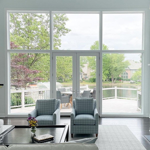 An expansive window wall with a view of a lake past a wooden deck