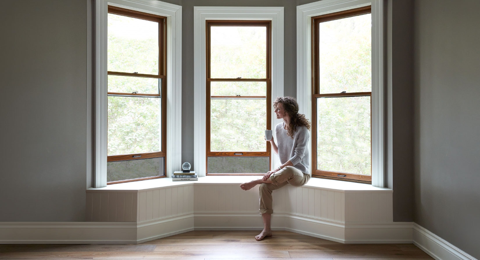 woman sitting in window seat by three double-hung windows forming a bay window