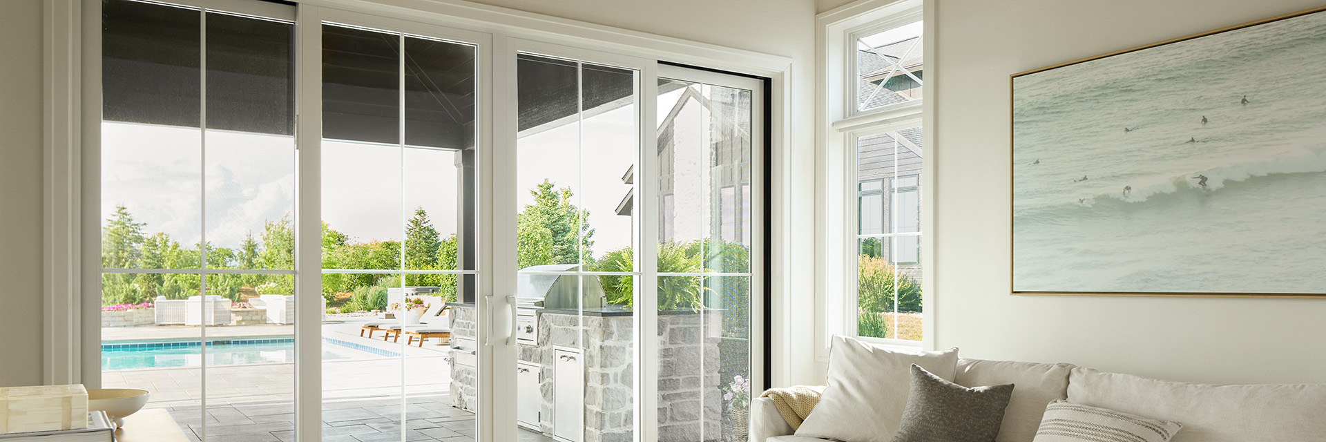 Elegant white sliding patio door with decorative grilles, opening to a backyard pool and outdoor kitchen, viewed from a bright modern living room. 