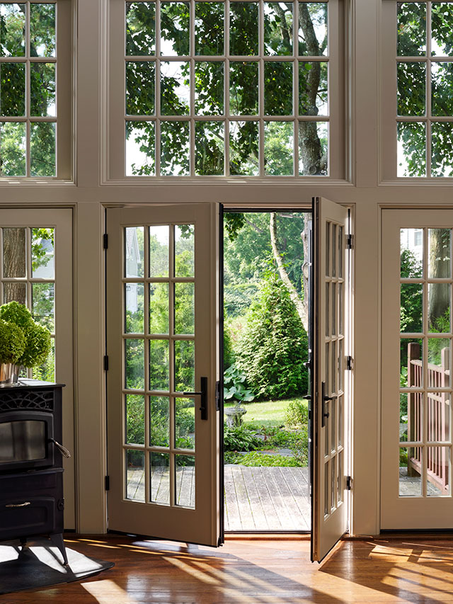 Dual colored patio doors open to a lush garden, framed by large windows and wooden flooring. 