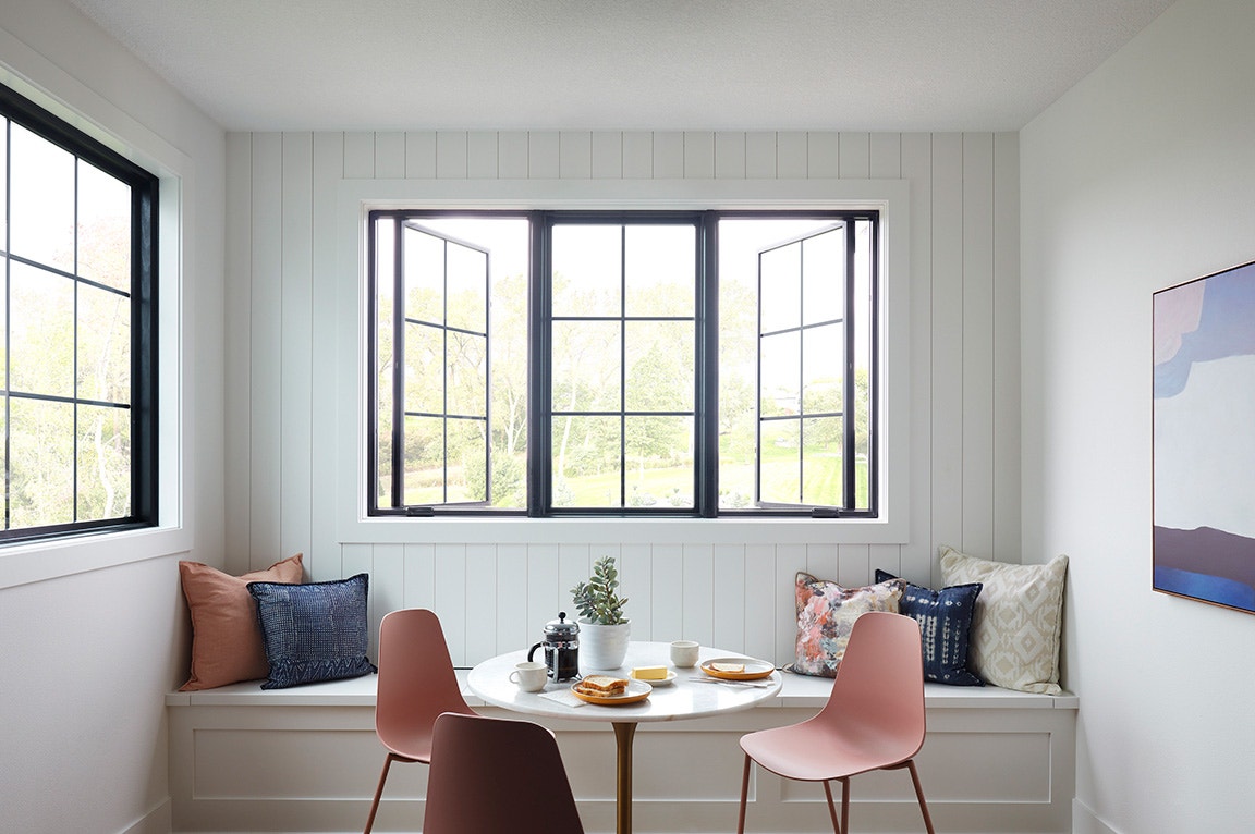 A modern dining area featuring a casement window with black frames, a round table, and stylish chairs.