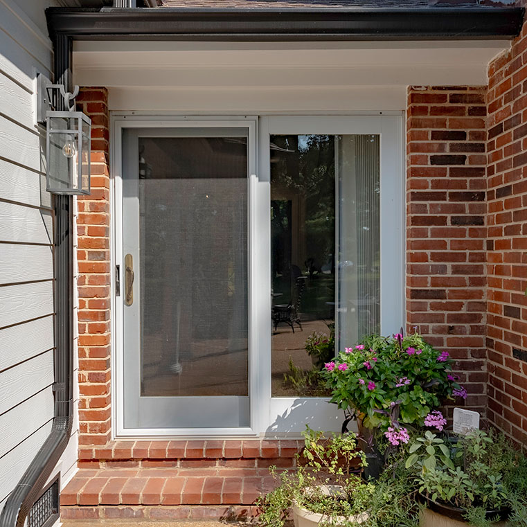 White sliding patio door with glass panels and silver handle on brick exterior.
