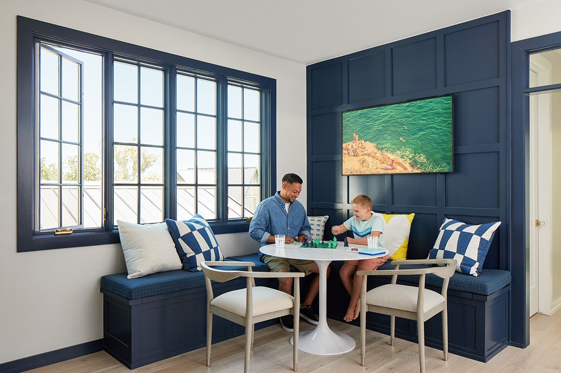 A modern living room with a blue casement window, featuring a family playing chess at a round table.